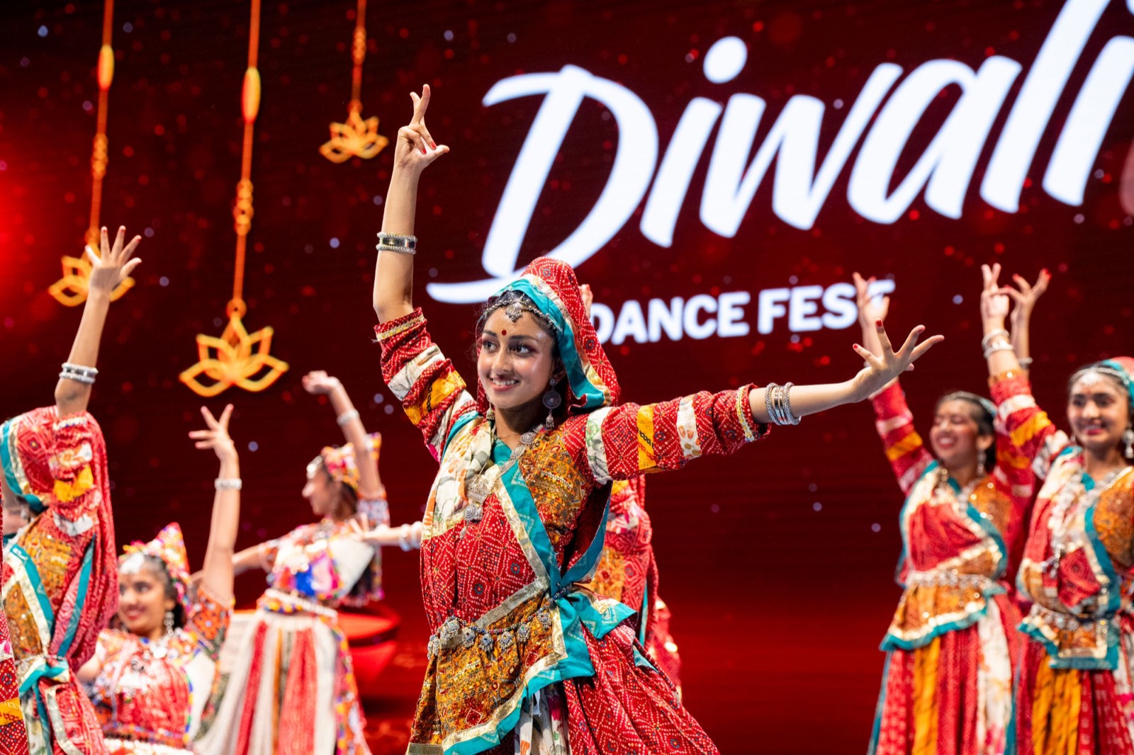 Dancers in red and teal traditional costumes performing in front of the Diwali Dance Fest screen